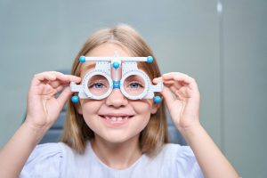Cheerful little girl undergoing eye exam with refraction test